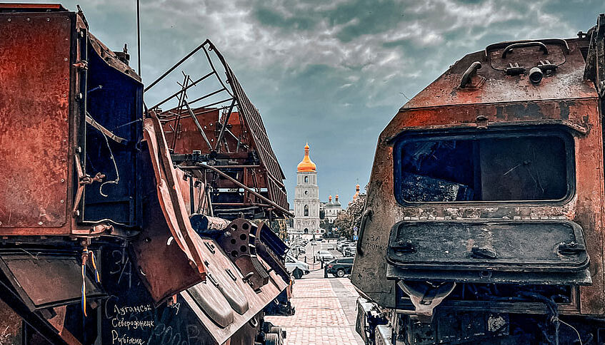 zerstörte Fahrzeuge vor einer Kirche in der Ukraine